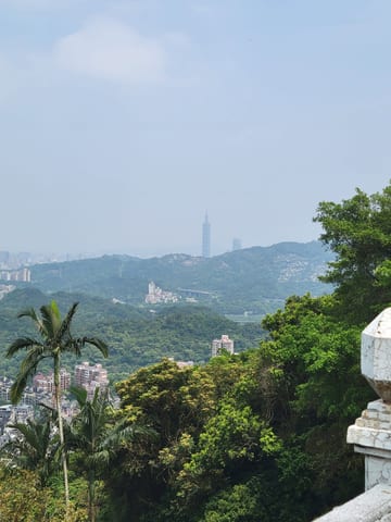 Taipei 101 visible beyond layered green hills from the temple
