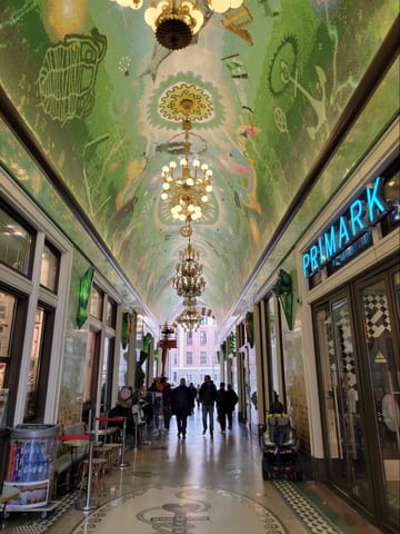 An ornate covered shopping arcade in Amsterdam with a painted ceiling and chandeliers