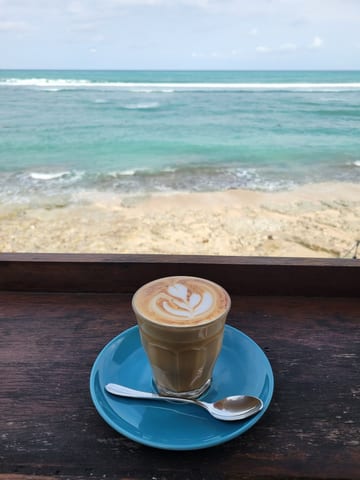 Hot coffee with latte art on a blue saucer overlooking Bingin Beach