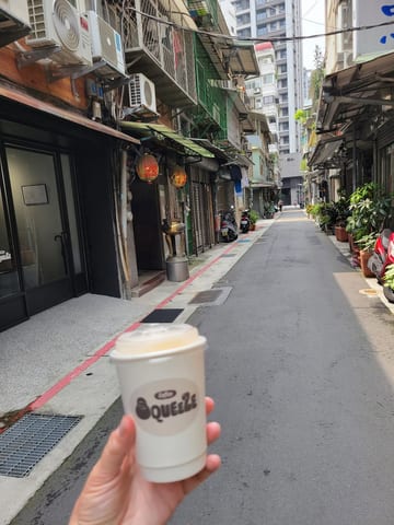 A takeaway coffee cup held up in a narrow Taipei alley