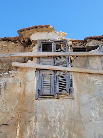 A weathered Larnaca building with cracked plaster, shutters, and exposed supports