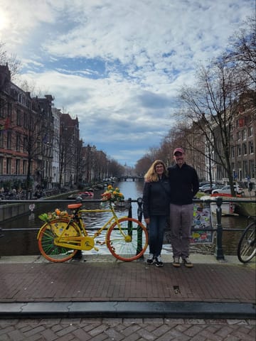 Two people standing beside a yellow bicycle at an Amsterdam canal