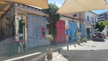 A sunny Larnaca old-town street lined with workshops, cafés, and colorful doors