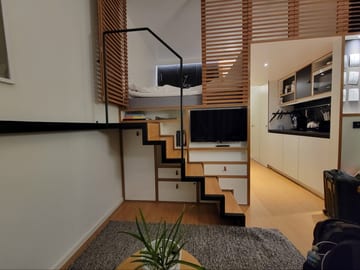A compact hotel room with a loft bed above a pull-out staircase