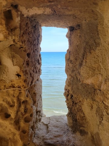 Blue sea and sky framed by a rough stone opening in Larnaca Fort