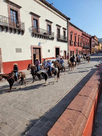 A group of cowboys riding horses down a sunny street in San Miguel de Allende