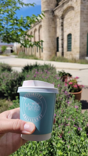 A hand holding a flat white in front of a historic stone building