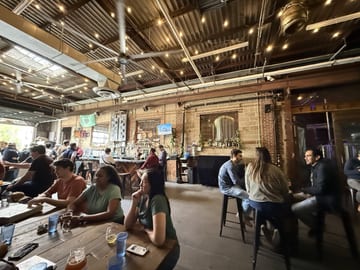 People sitting beneath lights inside Fifth Hammer Brewing
