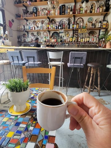 A small cup of Cypriot coffee held above a colorful mosaic table