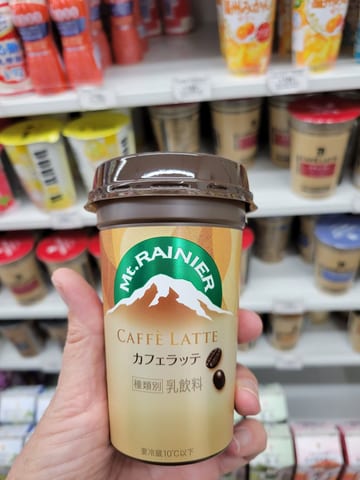 A hand holding a Mount Rainier Caffè Latte in front of a refrigerated store shelf