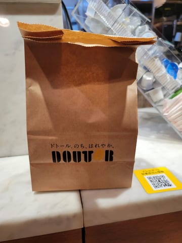 A takeaway coffee sealed inside a stapled paper bag at a Tokyo cafe