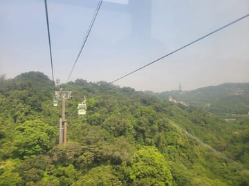 Gondola cabins crossing forested hills with Taipei 101 in the distance